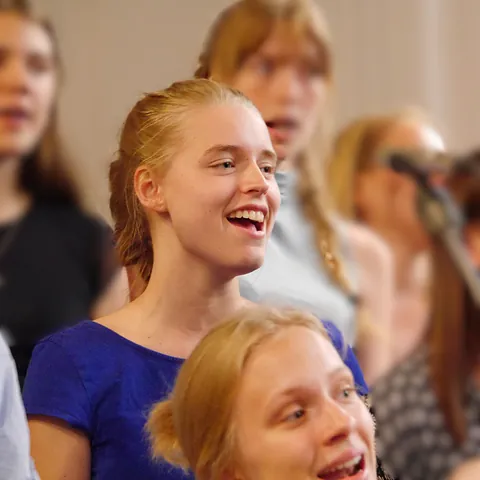 En smilende ung kvinde, der synger i et ungdomskor.