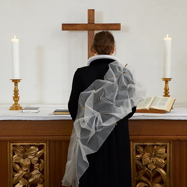 En præst set bagfra stående ved et alter med trækors.
