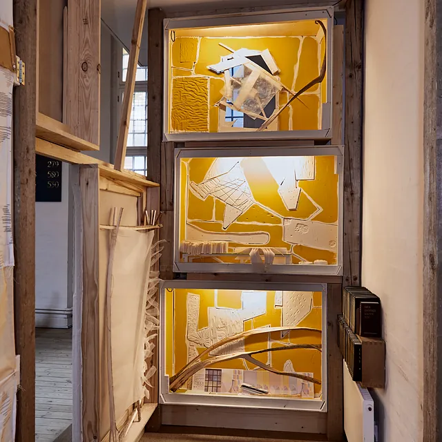 En kunstinstallation med tre oplyste, gule udstillingskasser.