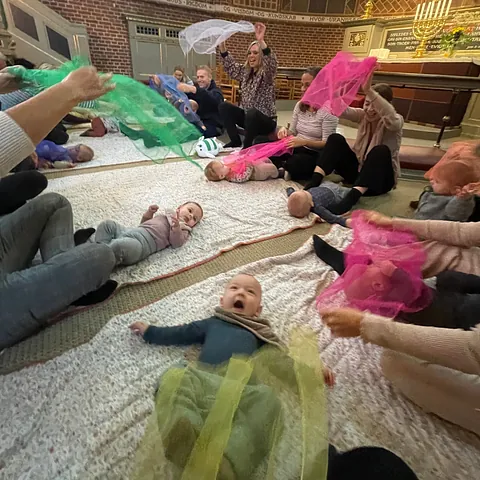 Forældre og babyer leger med farvede tørklæder til babysalmesang.