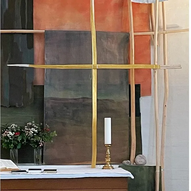 Et alter med et kunstnerisk trækors, et lys og blomster.